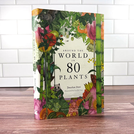 Book titled 'Around the World in 80 Plants' with colorful plant illustrations on a wooden surface.