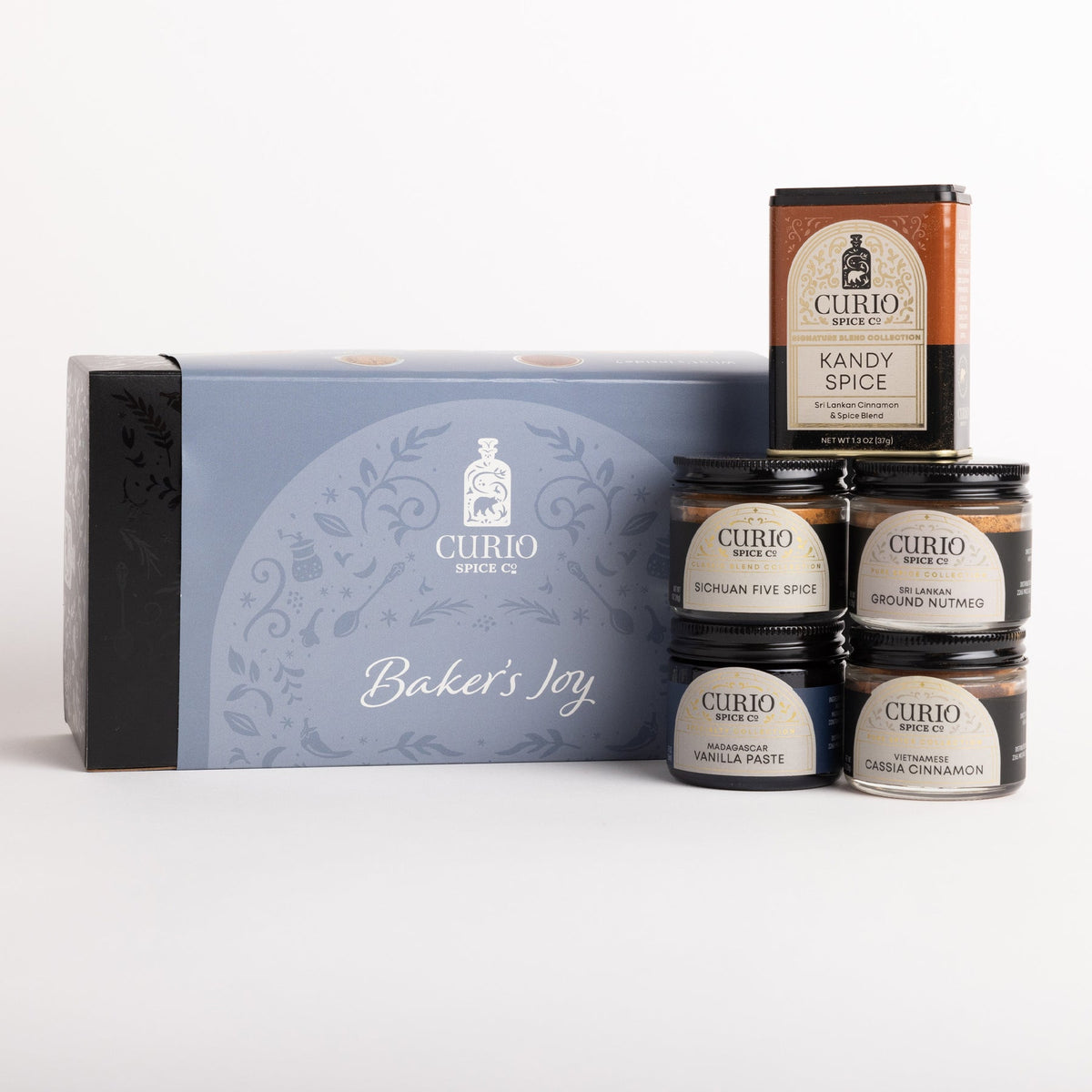 Curio Spice Gift Set featuring a light blue and black gift box labeled 'Baker's Joy' alongside five spice jars and one tin of Kandy Spice on a clean white background.