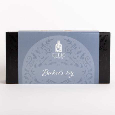 Curio Spice Co. 'Baker's Joy' spice box packaging, featuring a light blue central label with white decorative patterns and text, flanked by black sides, on a clean white background.