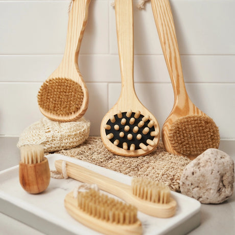 Set of wooden bath brushes and sponges on a white tray with a tiled wall background.