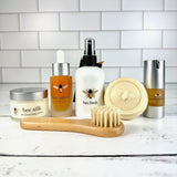 Collection of bee-themed skincare products on a white surface with a tiled wall background.