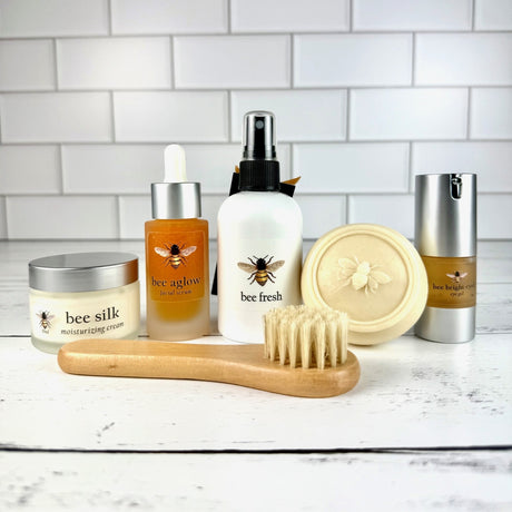 Collection of bee-themed skincare products on a white surface with a tiled wall background.