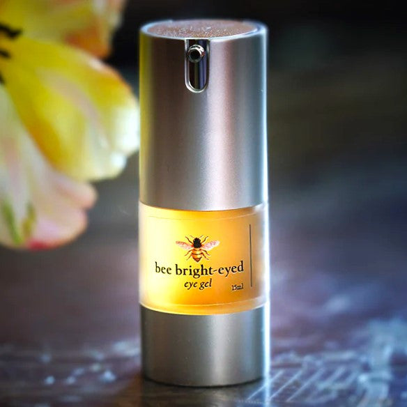 Bee Bright Eyed eye gel in a frosted bottle with silver bottom and silver pump top with illustrated bee label and text "bee bright-eyed"