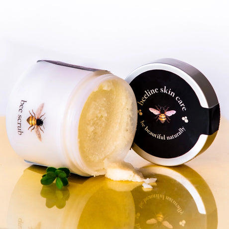Bee scrub with a container labeled 'Beeline skin care' on a reflective surface.
