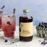 a bottle of Blueberry Lavender mixer alongside a prepared drink that is garnished with fresh blueberries and a sprig of lavender