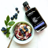 Bowl of yogurt with berries, a spoon, and a bottle of Runamok maple syrup on a white background
