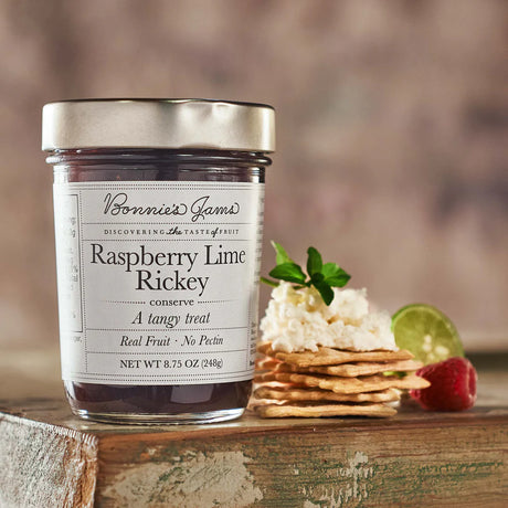 Jar of Raspberry Lime Rickey preserve with crackers and fruit on a wooden surface
