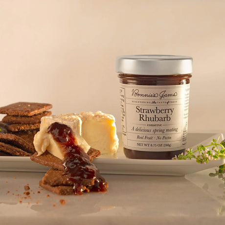 Jar of strawberry rhubarb jam on a plate with crackers and cheese