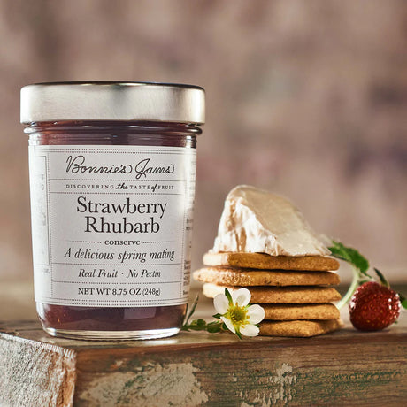 Jar of Bonnie's James Strawberry Rhubarb conserve with cookies and a flower on a wooden surface.