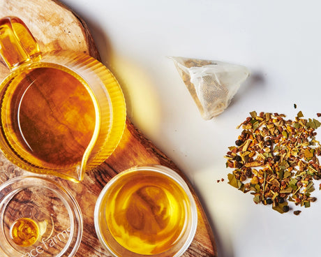 Tea leaves, a tea bag, and a glass of tea on a wooden board with a white background.