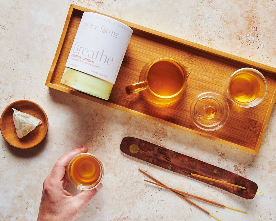 Tea-making setup with a wooden tray, tea bags, and a bottle labeled 'Breathe' on a textured surface.