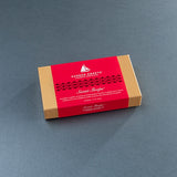 A rectangular box of Harbor Sweets' Sweet Slope chocolate, featuring a kraft brown cardboard body with a vibrant red paper band around the middle, set against a dark gray textured background.