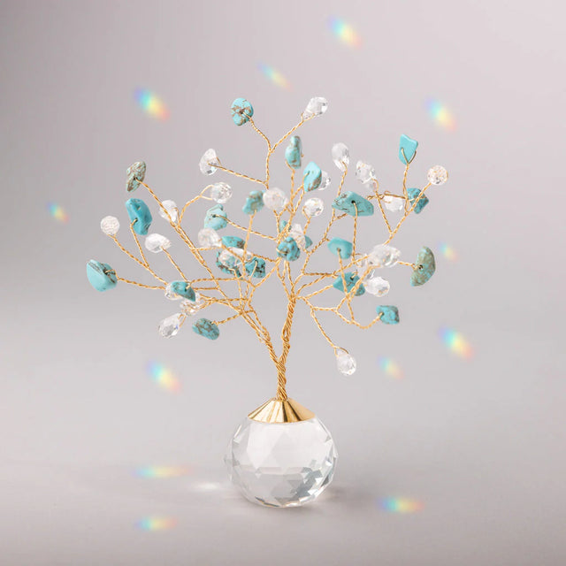 Decorative tree with gold branches and crystal base adorned with turquoise and clear crystals casting tiny rainbows against the light gray background