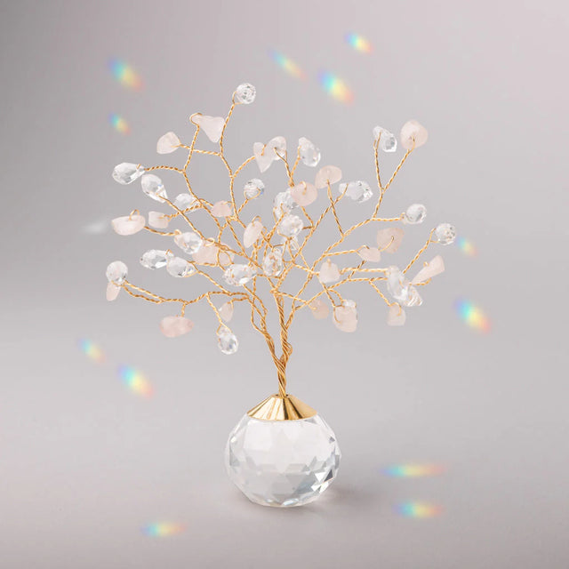 Decorative tree with gold branches and crystal base adorned with rose quartz and clear crystals casting tiny rainbows against the light gray background