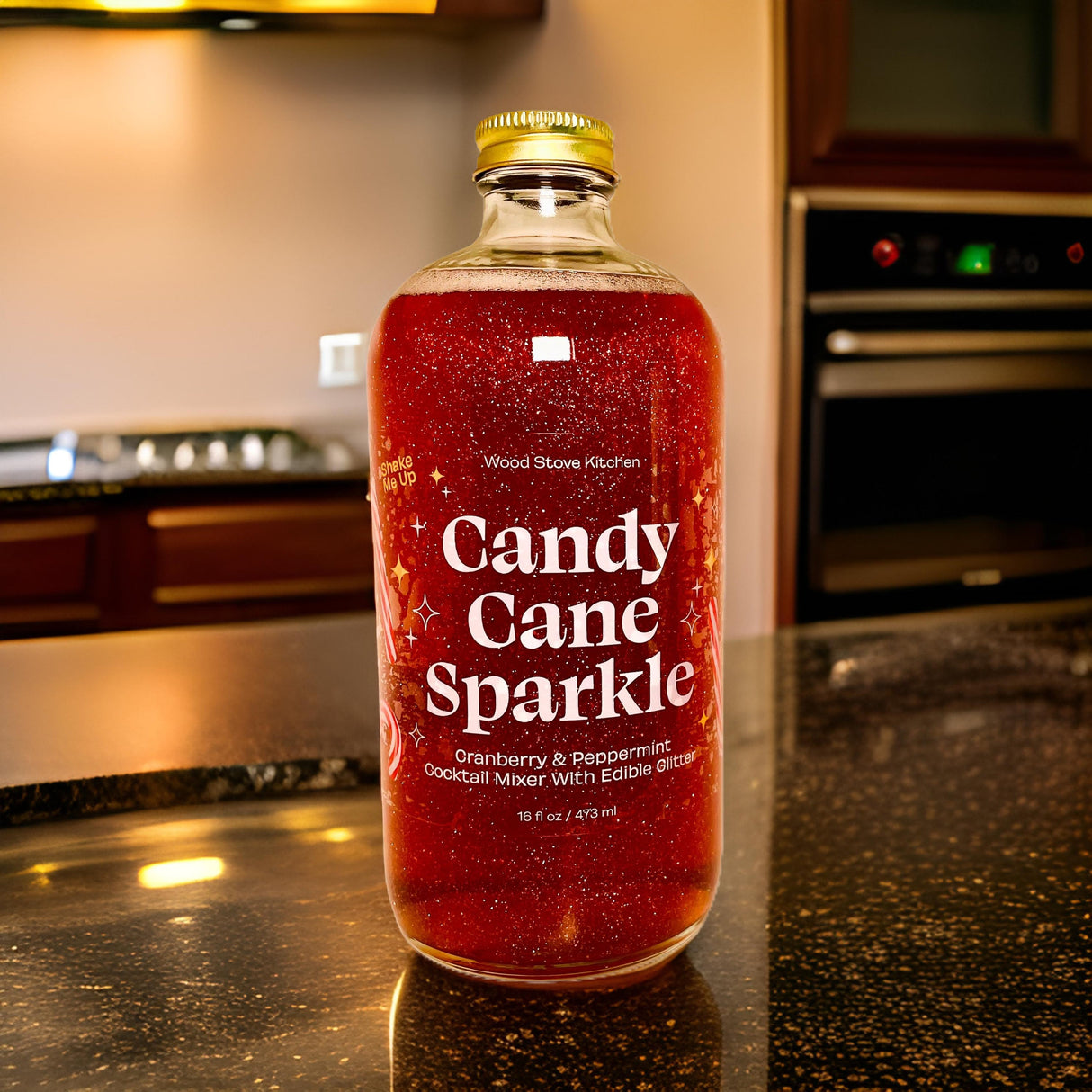 A bottle of 'Candy Cane Sparkle' cranberry and spicedew cocktail mixer with edible glitter, set on a dark kitchen countertop with a blurred kitchen background.