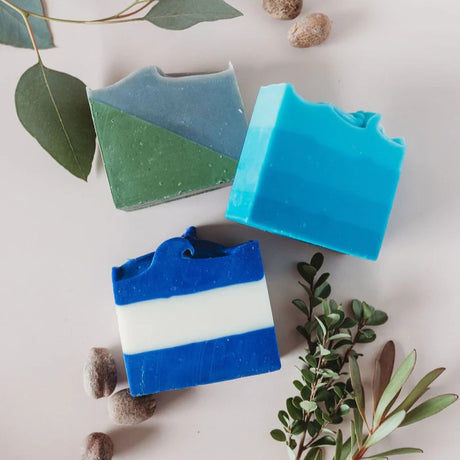 an above view of the 3 soap bars laying amongst herbs and elements of the fragrance in the soaps