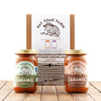 Two jars of Fat Toad Farm caramel sauce with a packaging box in the background on a wooden surface.