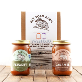 Two jars of Fat Toad Farm caramel sauce with a packaging box in the background on a wooden surface.