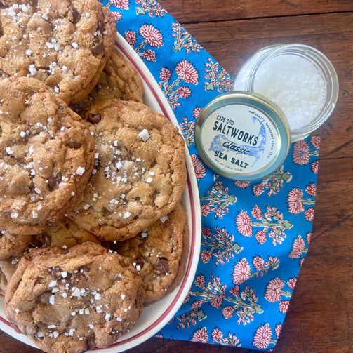 an open jar of classic sea salt next to a plate of cookies that are topped with flaky sea salt