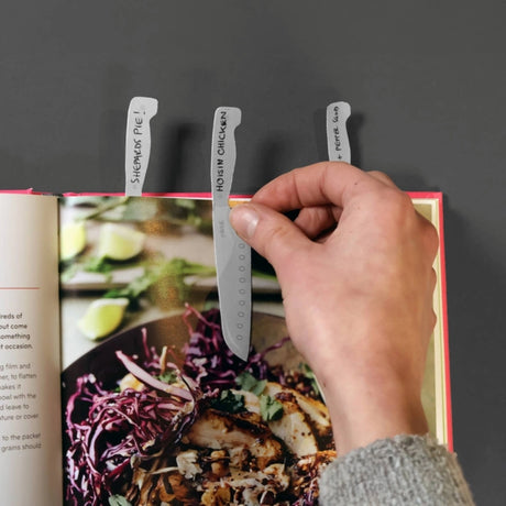 hand adding a cookmark to a recipe book page with other cookmarks on other pages