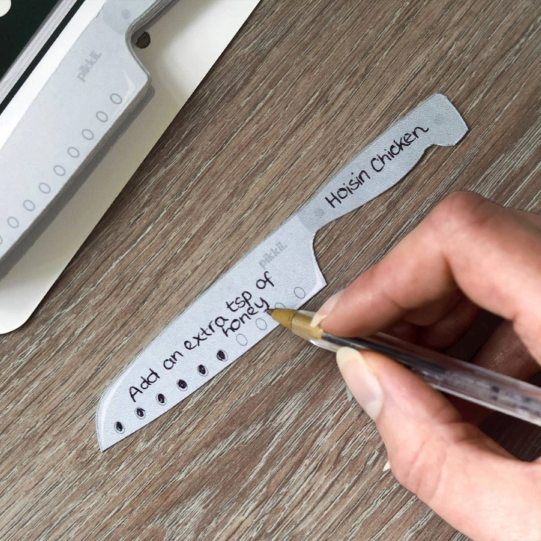hand holding a ball point pen and writing on the knife shaped cookmarks