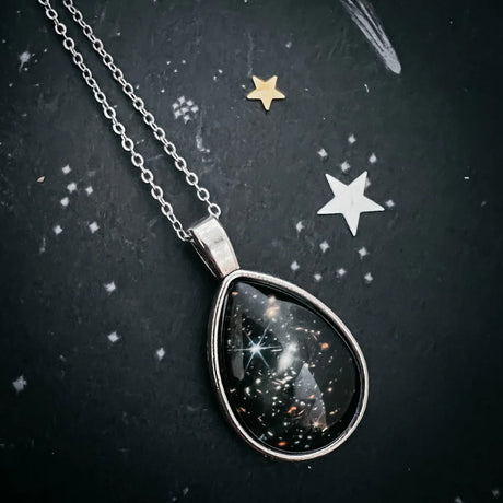 Teardrop-shaped necklace pendant with celestial design on a dark background