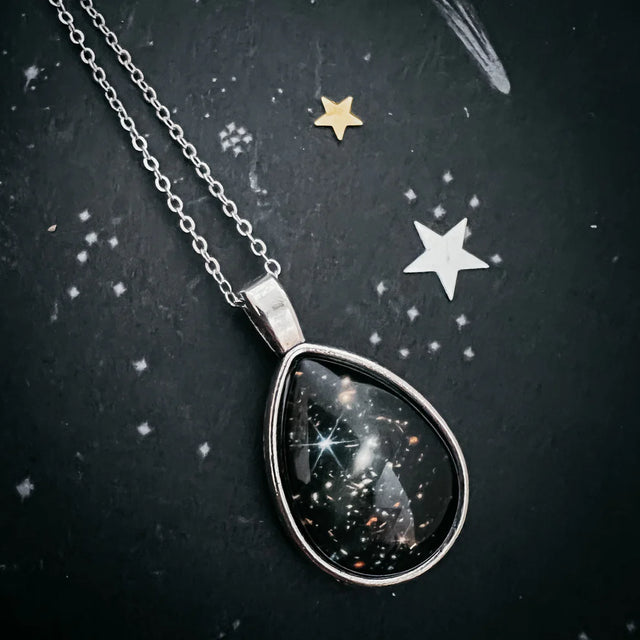 Teardrop-shaped necklace pendant with celestial design on a dark background