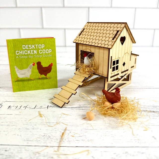 Wooden desktop chicken coop with a book titled 'Desktop Chicken Coop' on a white wooden surface.