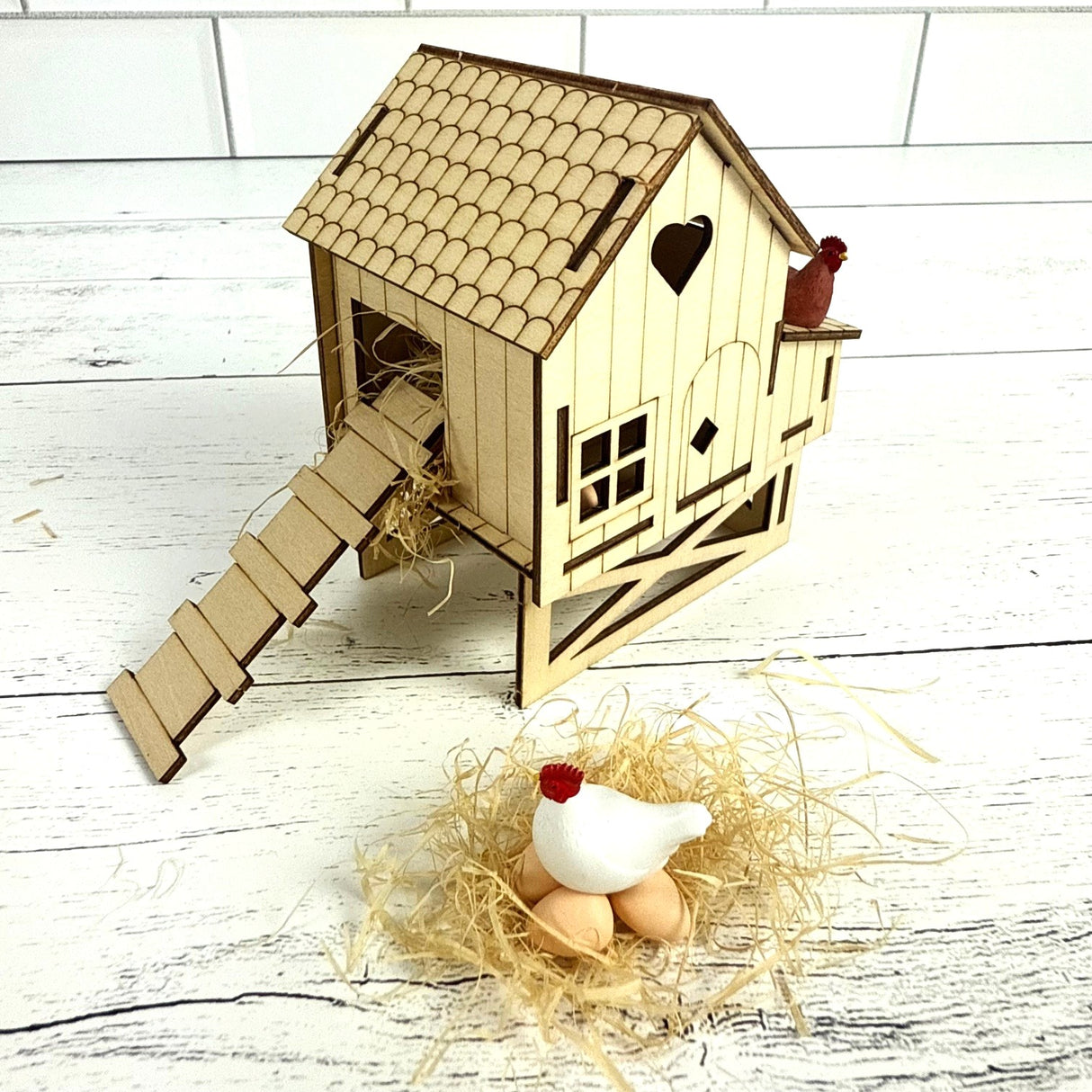 Wooden chicken coop model with a small chicken and eggs on a white wooden floor.