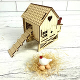 Wooden chicken coop model with a small chicken and eggs on a white wooden floor.