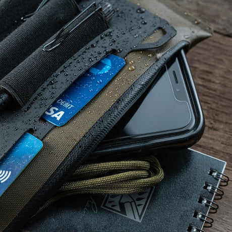 a close up of the pouch with the zipper pouch open with a phone, charging cable, and top spiral notebook poking out of the pouch showing the storage capacity