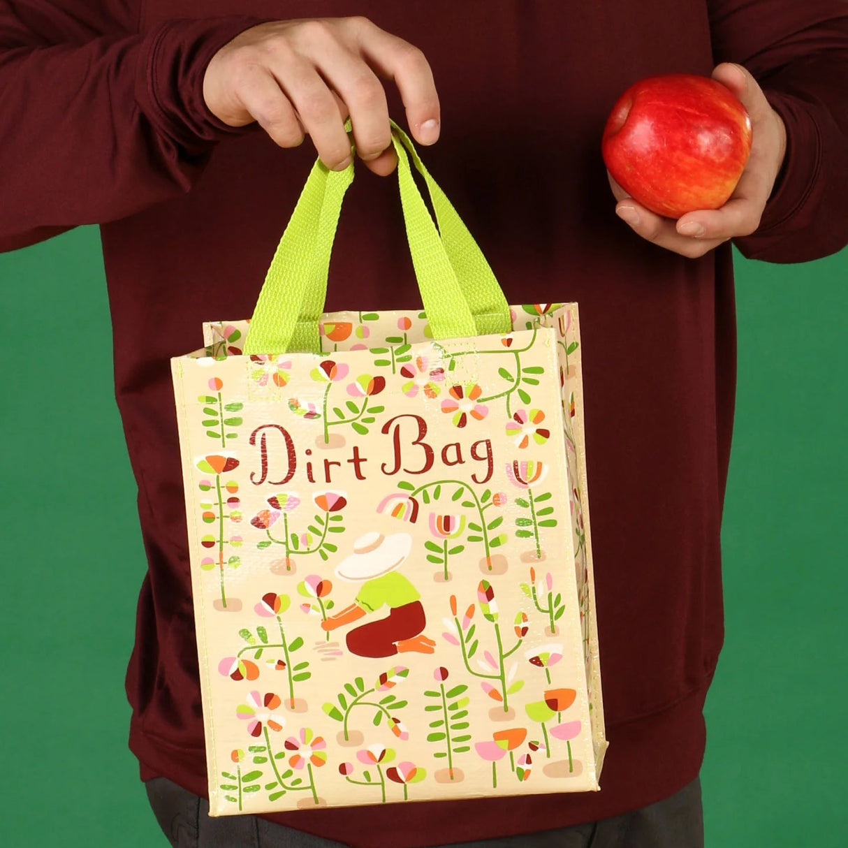 Person holding a 'Dirt Bag' bag with a colorful design and an apple against a green background
