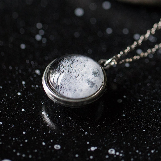 Silver necklace with a round moon pendant on a dark background