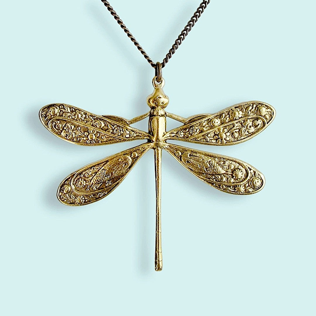 Gold dragonfly pendant with floral motif on the wings on a chain against a light blue background