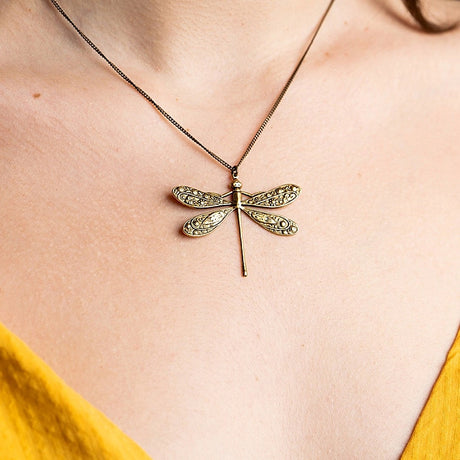 Gold dragonfly necklace on a person wearing a yellow top