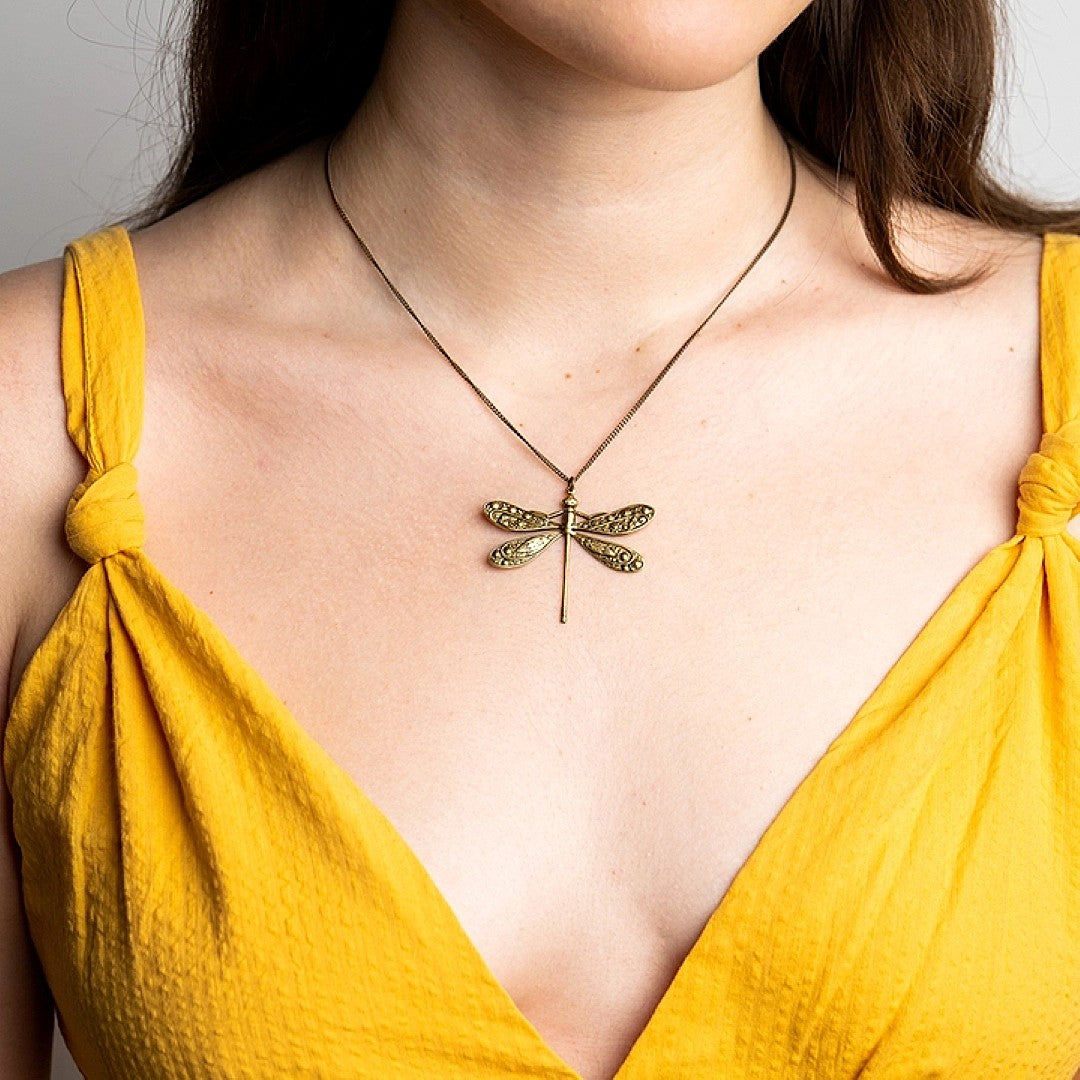 Woman wearing a yellow top with a dragonfly pendant necklace.
