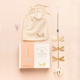 Gold dragonfly suncatcher with packaging, suction cup, and drawstring bag on a beige background