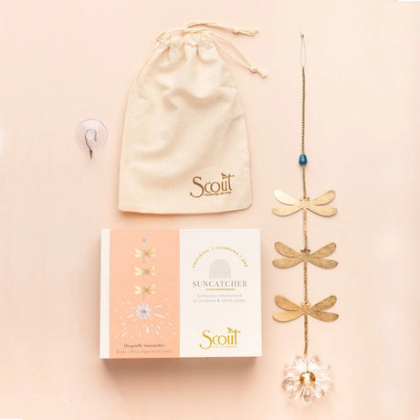 Gold dragonfly suncatcher with packaging, suction cup, and drawstring bag on a beige background