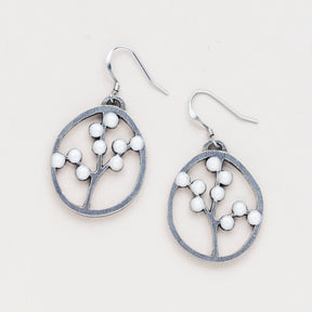 a pair of oval pewter earrings with branches inside adorned with white beads to represent blossoms