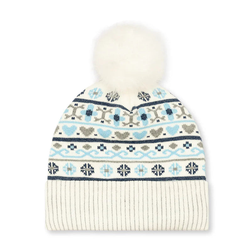 A cream-colored knit beanie hat featuring a white faux fur pom-pom on top and a colorful Fair Isle pattern with light blue, navy, and gray motifs on the upper section, finished with a solid cream ribbed cuff.