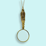 Gold magnifying glass pendant on a light blue background