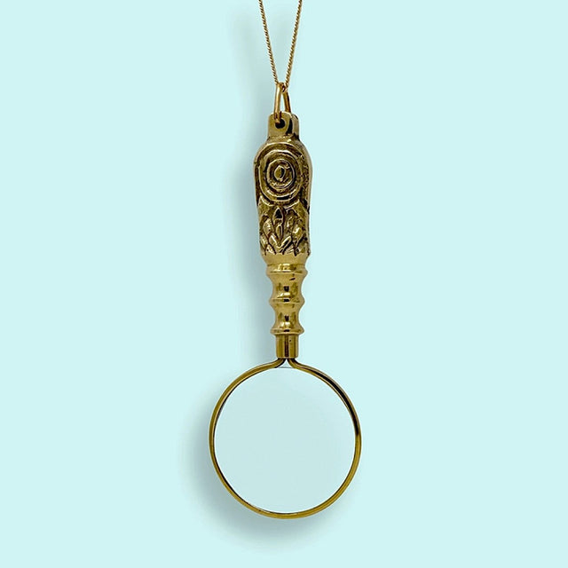 Gold magnifying glass pendant on a light blue background