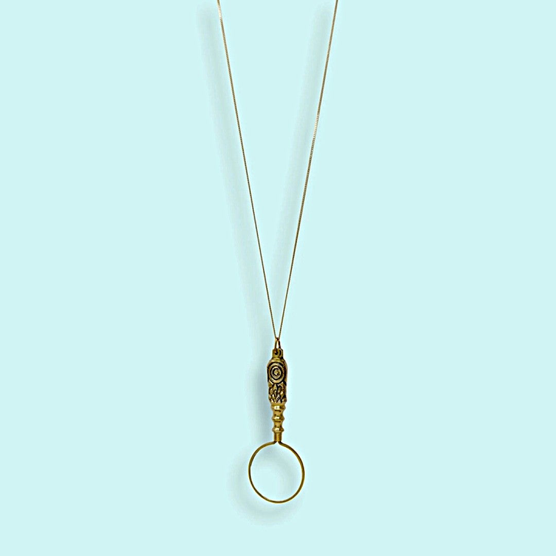Gold magnifying glass pendant with brass chain on a light blue background