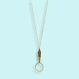Gold magnifying glass pendant with brass chain on a light blue background