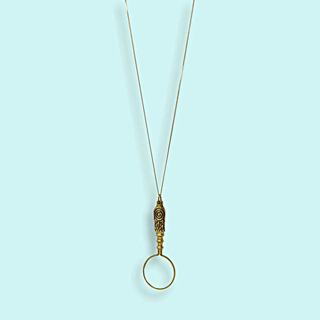 Gold magnifying glass pendant with brass chain on a light blue background