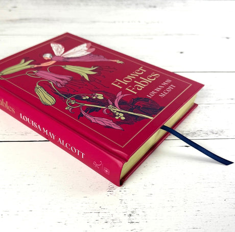 Book titled 'Flower Fables' by Louisa May Alcott with floral design on a white wooden surface