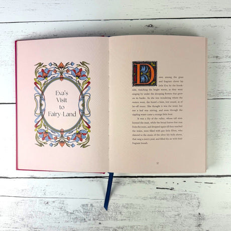 Open book with decorative text and illustrations on a wooden surface