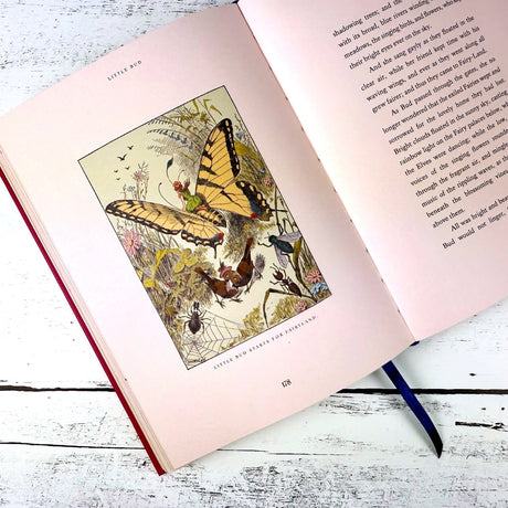 Open book with a colorful illustration of a fairy riding a butterfly in a garden with insects and birds on a white wooden surface