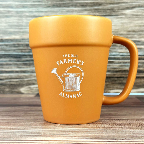 terracotta style mug with 'The Old Farmer's Almanac' logo and vintage watering can graphic on a wooden surface.