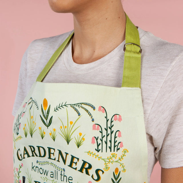 Person wearing a light green apron with floral designs and text against a pink background